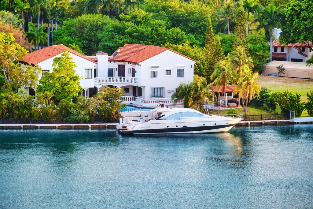 Elegant Miami luxury villa by the waterfront with a yacht docked nearby, unique architecture and tropical setting.